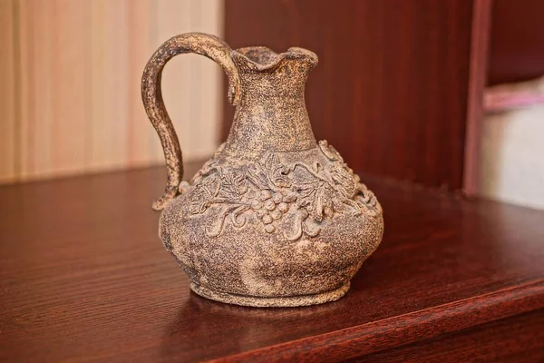 one old brown ceramic vase with a pattern stands on a red table in the room