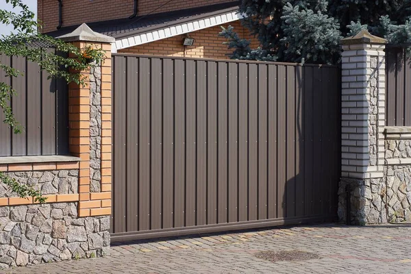 Büyük, kapalı, kahverengi bir kapı. Tuğladan bir duvarın üzerinde. Gri bir kaldırımın üzerinde.