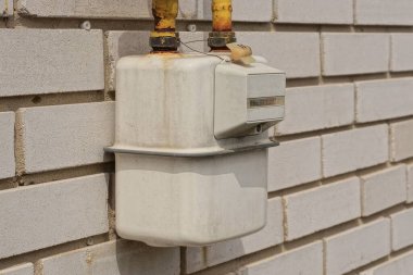 one white metal gas meter with yellow iron pipes on a gray brick wall of a house on the street