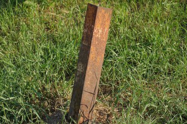 Yaşlı, kahverengi, paslı demir bir direk sokağın yeşil çimlerinde duruyor.