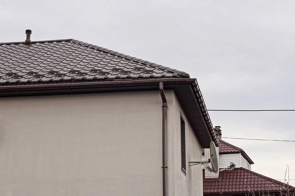 part of a private house made of concrete attic with windows under a brown tiled roof against a gray sky