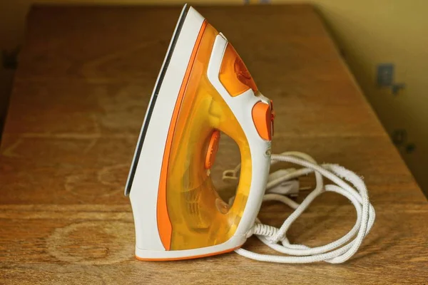 Jedna Bílá Oranžová Elektrická Žehlička Drátem Stojí Hnědém Stole Místnosti — Stock fotografie