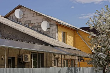 Beyaz sarı tuğlalı özel ev gri bir çatı altında mavi gökyüzüne karşı çitin arkasında.