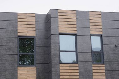 Siyah bir duvardan bir evin tavan arası ve caddelerde camları olan kahverengi ahşap tahtalar gri gökyüzüne karşı.