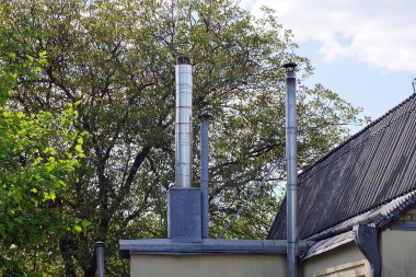 Mavi gökyüzüne ve ağaç dallarına karşı tahta çatıdaki iki uzun gri baca borusu.