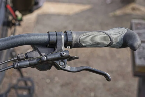 Siyah metal bir gidonun parçası. Plastik saplı ve frenli. Sokakta kablo var.