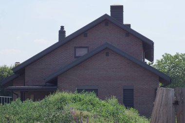 Sokakta gökyüzüne karşı yeşil çimenler içinde özel tuğlalı kahverengi bir evin cephesi