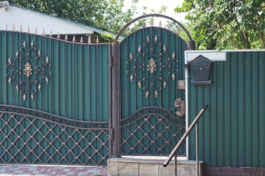 Gri bir kaldırımda siyah dövmeli, kapalı yeşil metal bir kapı.