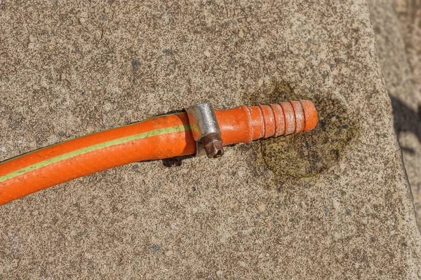 街上的一个灰色混凝土桌子上躺着一个装有金属夹钳的湿塑料橙色软管的一部分 — 图库照片
