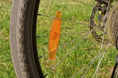  Siyah bisiklet tekerleğinin gri metal tellerindeki kırmızı plastik yansıtıcı sokaktaki yeşil çimlerin arka planına karşı.