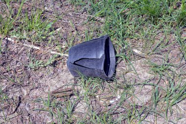 Siyah kırık plastik bir saksının çöpü yerde yatıyor ve doğada yeşil çimenler var.