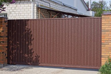 Büyük, kahverengi bir metal kapı ve sokaktaki çitlerin bir kısmı.