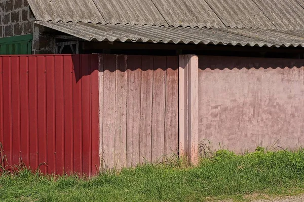 gray slate roof on red metal fence of pink wooden planks and concrete wall in green grass outdoors