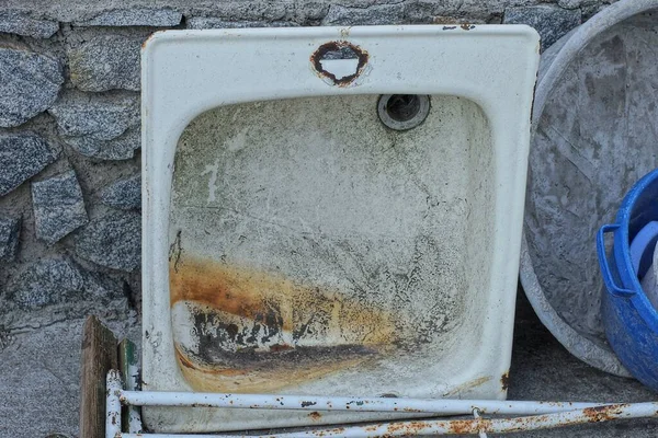 街上的一堵石墙映衬着一个生锈的白色金属脏厨房的旧水池 — 图库照片