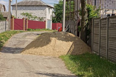 Çitin gri beton duvarının yanındaki yeşil çimlerin içinde büyük kahverengi kum yığını.