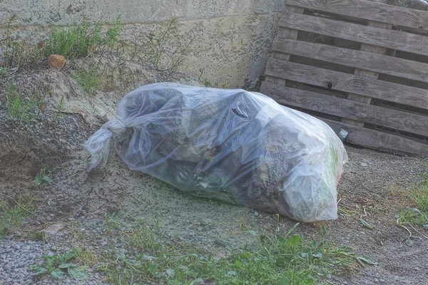 one large white plastic garbage bag lies on the gray ground outside
