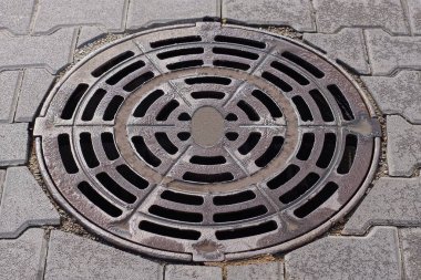 Kanalizasyondan çıkan kahverengi, nemli bir rögar kapağı sokağın gri kaldırımında yatıyor.