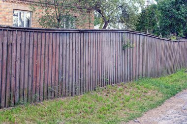 Kırsal sokaktaki tahtalardan kalma eski, kahverengi, ahşap bir duvar çiti.