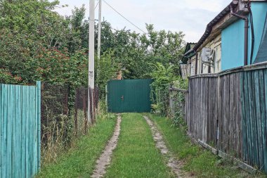 Kırsal sokak, yeşil çim yolu gri ahşap çitler ve demir kapılı metal çitler.