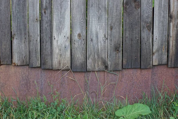 texture from an old fence wall made of gray wooden planks and rusty brown metal outdoors in green grass