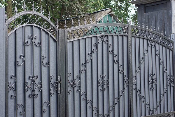 gray metal door and large closed gate with black wrought iron pattern with sharp bars on a rural street