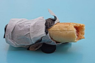 Sosisli sandviç, kırmızı ketçap, siyah kağıt ambalajda ekmek ve mavi bir masanın üzerinde beyaz peçete.