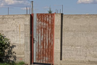 açık havada gri beton bir duvarda mavi gökyüzüne karşı kapalı kahverengi metal bir kapı.