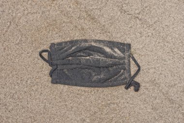 one old black dirty medical mask lies on the gray sand in the street