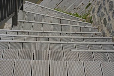 part of a gray staircase with iron steps on a city street against a wall