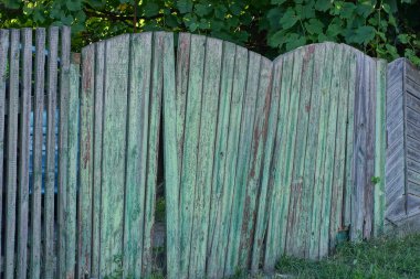 one old closed wooden green gate with a broken board on a gray fence in a rural street