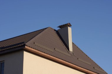 one gray chimney on the brown tiled roof of a private house against the blue sky