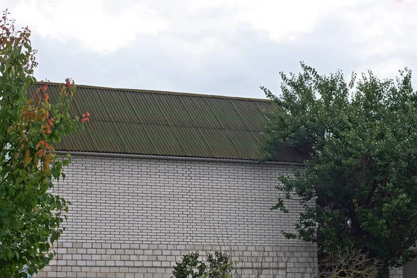 wall of a white private brick house under a green slate roof on the street against a gray sky among the trees