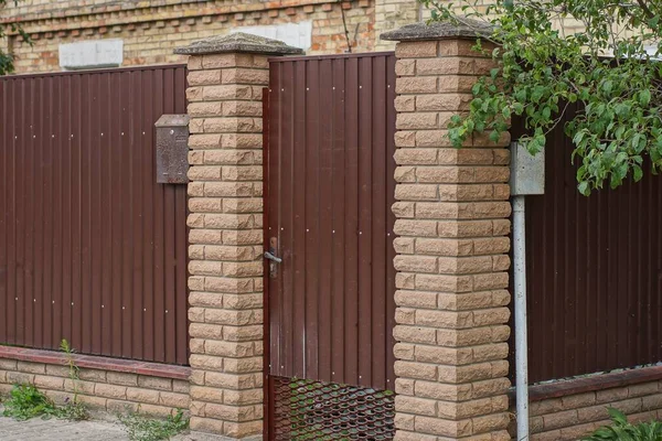 one closed iron brown door and part of a wall fence made of bricks and metal on a rural street