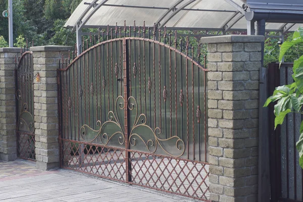 one black metal gates a brown forged pattern and part of a brick gray fence on the street