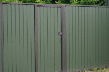 a one green metal door and a fragment of a wall fence on a rural street