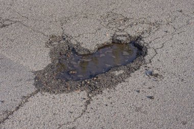 one small pit pothole with dirty water on the gray asphalt road on the street