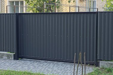 Büyük, kapalı bir metal kapı ve kırsal bir sokakta demir çitin bir parçası.