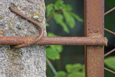 gray concrete pole on a metal mesh fence with rusty brown rod outdoors near green vegetation
