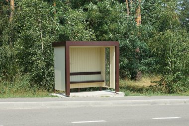 one empty plastic brown bus stop on the street near the gray asphalt road against the background of green vegetation