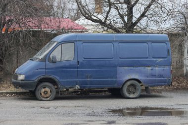 one old blue minibus car stands on a gray wet asphalt road in the street