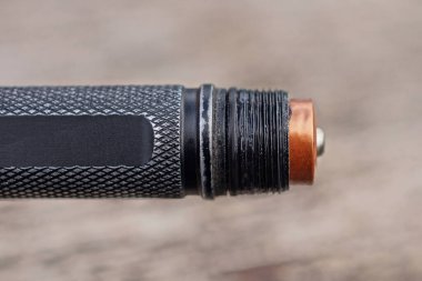 part of one black small metal flashlight with a brown battery on a gray background