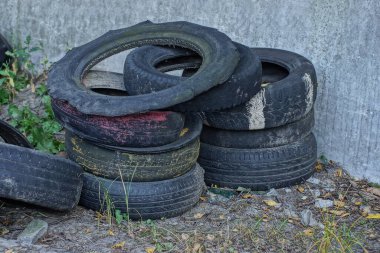 Gri zeminde ve sokaktaki yeşil çimlerde bir sıra siyah araba lastiği.