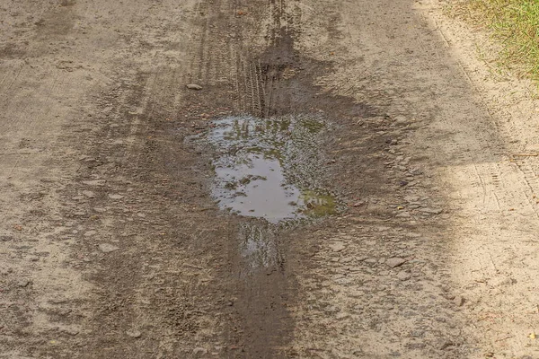 田舎道の灰色の地面に茶色の汚れた水で1つの水たまりがあり — ストック写真