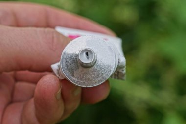 hand holds one gray metal tube with white ointment on a green background