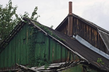 old green black wooden loft of a rural house with a chimney on the street against the sky