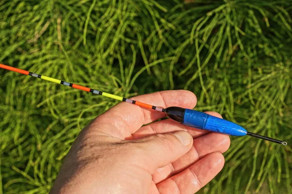 Hand Holds One Long Plastic Colored Fishing Float Background Green — Foto de Stock