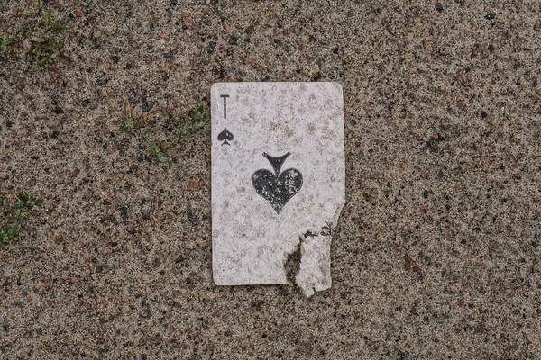 one dirty torn playing card ace of spades lies on the gray ground in the street