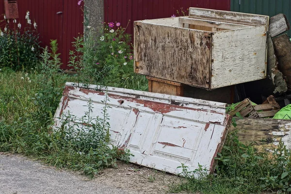 a pile of garbage from old white wooden doors and gray boxes stand on the ground and green grass on the street