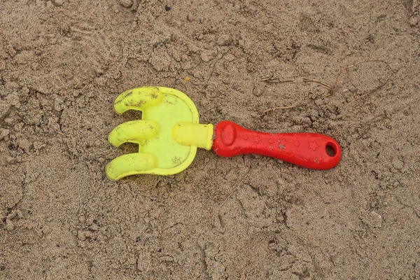 Ένα Μικρό Χρωματιστό Πλαστικό Παιχνίδι Τσουγκράνα Βρίσκεται Στην Γκρίζα Άμμο — Φωτογραφία Αρχείου