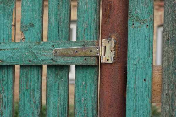 one gray metal door hinge on a brown rusty iron post and green planks of a wooden door outside